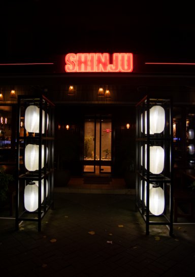Eingang zu einem Restaurant mit leuchtendem "Shinju"-Schild und Papierlaternen.