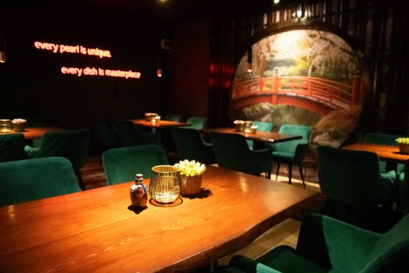 Gemütliches Restaurantinterieur mit Holztischen, grünen Stühlen und dekorativer Wandmalerei.