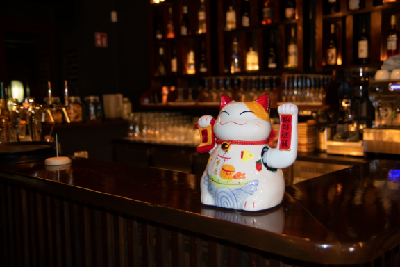 Ein Glückskatzen-Statuette steht auf einer Theke vor einer Bar.